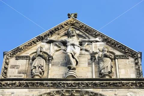 Close-up of crucifix on top of stone church peaked facade with blue sky Stock Photos