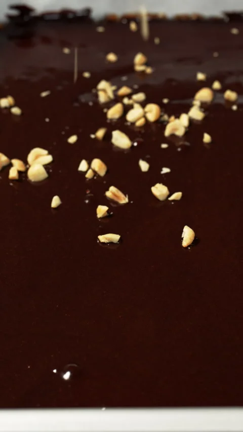Close-up of crushed peanuts being sprinkled on liquid chocolate ganache Stock Footage 329070084