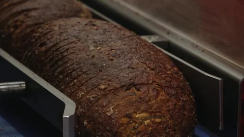 Close-up of a crusty dark bread loaf being sliced on bakery equipment, showing Stock Footage 335936337