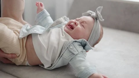 Close-up of a crying baby with a bow on its head lying on a sofa Vidéo 340580917