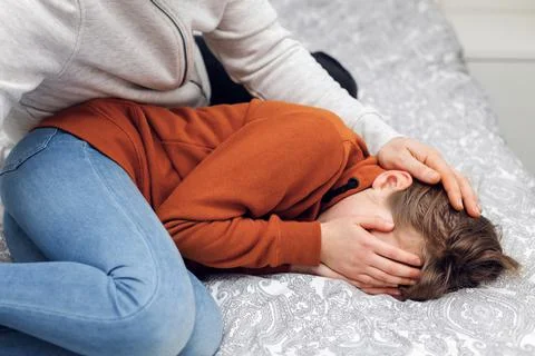 Close-up of a crying child lying on the bed and the father's hand stroking her Stock Photos