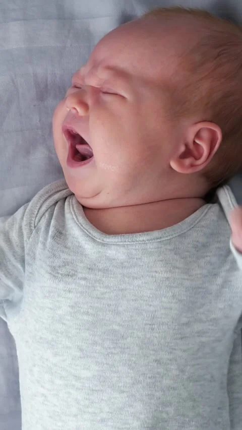 Close up of crying newborn baby boy with tearful face lying on a gray bed sheet Video stock 341285740