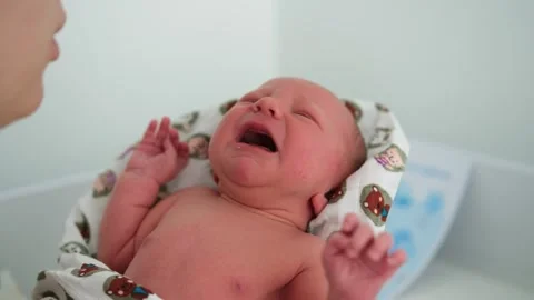 Close-up of a crying newborn baby held in his mother's arms, as she gently 库存影片 344771990