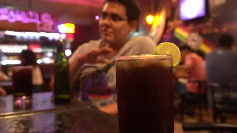 Close-up of a cuba libre at a bar table with a man in the background chatting wi Stock-Footage 196736739