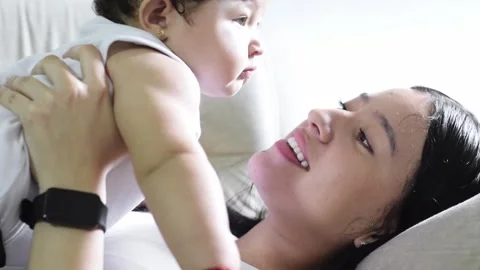 Close cuddle: single Latina mother lying on the sofa with her baby girl, ki.. Stock Footage 321315502