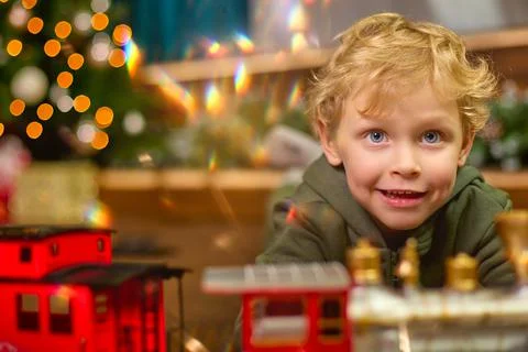 Close-up of a curly-haired boy playing with magic toy train at Christmas tree. Stock Photos