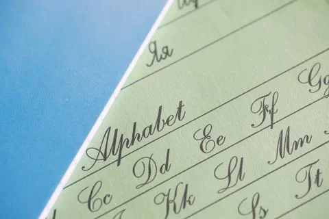 Close-up of Cursive Alphabet Chart on Green Paper with Blue Background Foto stock