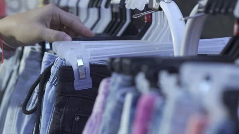 Close-up of a customer hand browsing and selecting trousers on a clothing rack Stock Footage 335562314