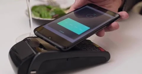 Close-up customer hand uses smartphone to make a wireless payment nfc technology Video stock 336585619