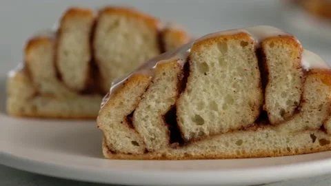 Close-up cut of cinnamon rolls on a plate. Sweet cream cheese frosting pouring Stock Footage 141375045