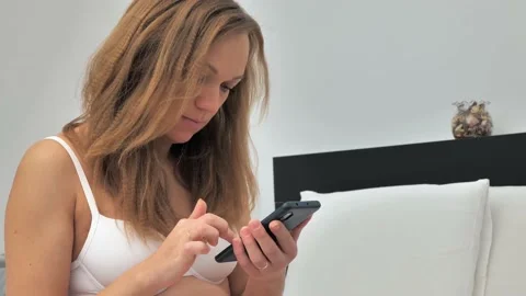 Close-up of a cute blonde sitting on a sofa and holding a phone. She looks at Stock Footage 228993855