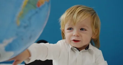 Close up of the cute funny small boy spinning a big globe in front of him. blue Stock Footage 82917968