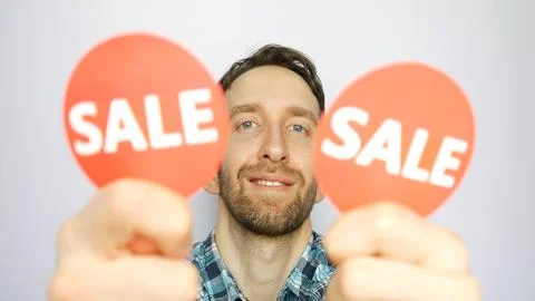 Close-up of a cute man showing two defocused red round signs with the words SALE Stock Photos