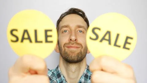 Close-up of a cute man showing two defocused yellow round signs with words SALE Stock Photos