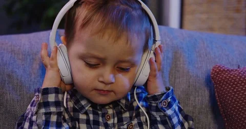 Close up of the cute small boy sitting on the grey couch and listening to the Stock Footage 82920183