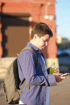 A close up of cute student boy with backpack holds a mobile phone and bottle of Foto stock