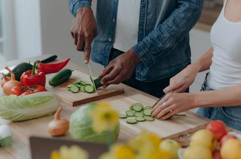Close up of a cutting board with the hands of a couple cutting vegetables t.. Stock Photos