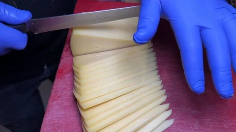 Close-up of cutting cheddar on board. Attendant slicing cheese at the deli co Stock Footage 237432418