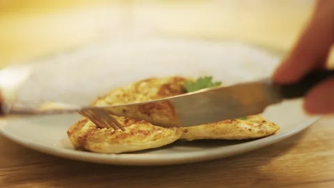 Close-up cutting grilled chicken breast, hand, plate, restaurant table, warm lig Video stock 321193181