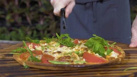 Close up cutting pizza on slices with roller knife on wooden table in pizzeria Stock Footage 99170031