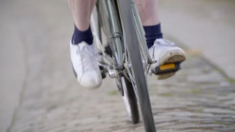 Close-up of a cyclist's legs pedaling an old, rickety bicycle on a bumpy Stock Footage 299228114