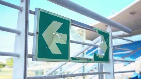 Close-Up of Damaged Directional Signage on Stadium Railing With Blue Seats in 動画素材 346654064