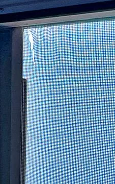 Close up of a damaged window screen with blue sky background showing small .. Stock Photos