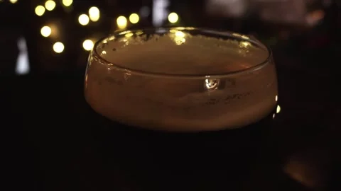 Close up of dark beer glass with thick foamy head, showcasing golden bokeh Stock Footage 335762621