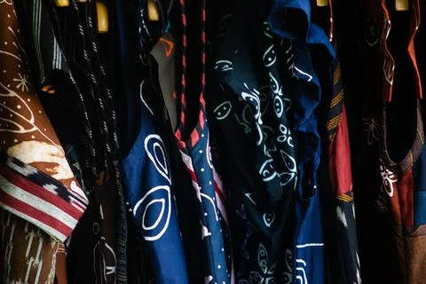 Close up of dark blue and patterned batik fabrics hanging in a rack showcas.. Stock Photos