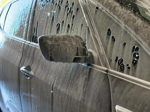 Close-up of a dark car covered in thick active white cleaning foam during a.. Stock Photos