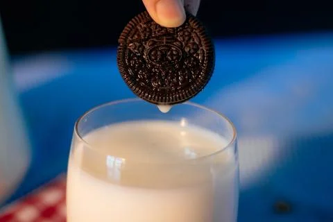 Close-up of a dark chocolate cookie being dipped into fresh white milk Stock Photos