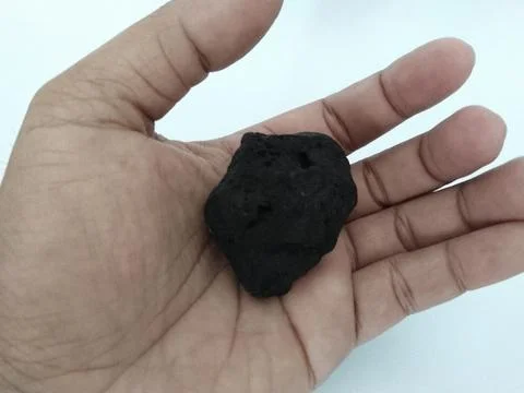 Close-up of a dark coal held in a person's palm against a white background Stock Photos