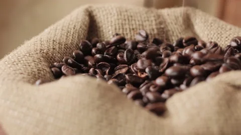 Close-up of dark coffee beans falling from above into an eco-friendly burlap bag Stock Footage 154219768