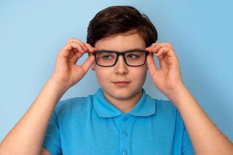 Close up of dark haired boy in glasses on light-blue background, looking away Stock Photos
