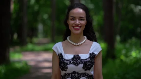 Close-up of a dark-haired curly-haired young smiling girl walking in a green 스톡 동영상 134841947