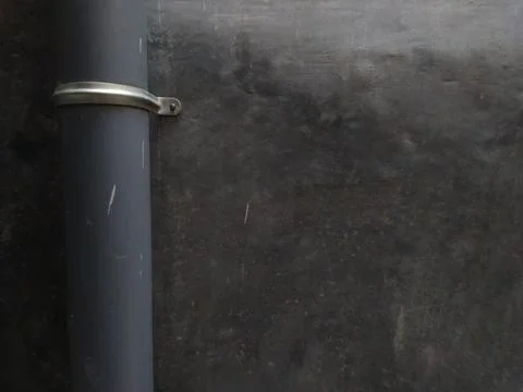 Close-up of a dark pipe secured to a textured wall with a metal clamp. Stock Photos