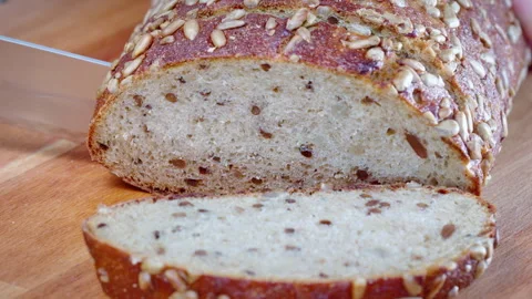 Close-up of dark seeded bread being sliced with a bread knife on a wooden board. Video stock 302633449