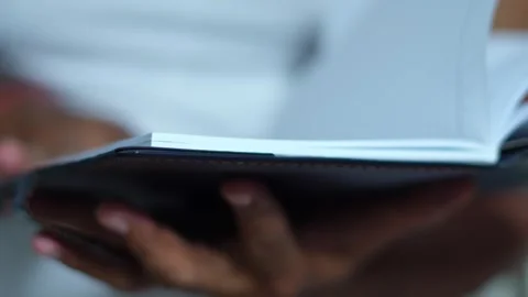 Close up of dark skinned hands leafing through the pages of a leather bound Stock Footage 345189028