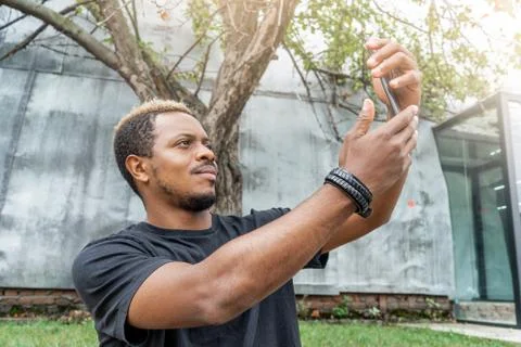 Close up of dark-skinned man in black T-shirt making selfie on mobile phone. Stock Photos
