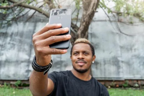 Close up of dark-skinned man in black T-shirt making selfie on mobile phone. Stock Photos