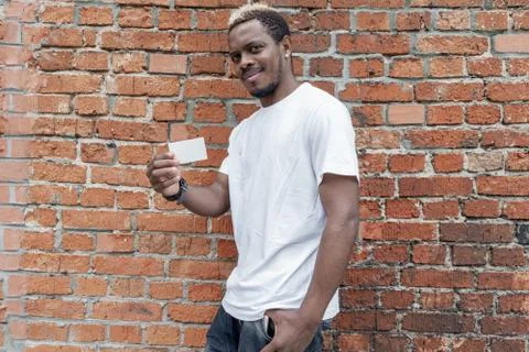 Close up of dark-skinned man in white T-shirt showing blank business card. Stock Photos