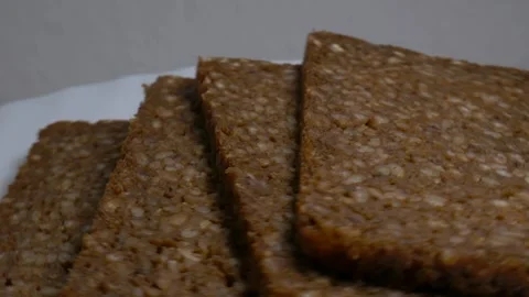 Close-up of dark whole grain rye bread slices rotating on a white plate, sh.. Stock Footage 346296600