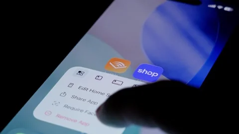 Close-up of deleting the Shop app from an iPhone home screen in a dark setting Stock Footage 334059910