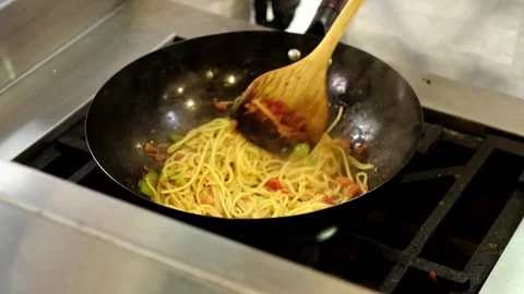 Close-up of a delicious pasta dish being stir-fried in a wok over a gas stove Stock Footage 314324611
