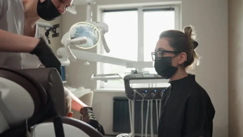 Close up dental assistant assisting patient in modern clinic with overhead light Stock Footage 345834466