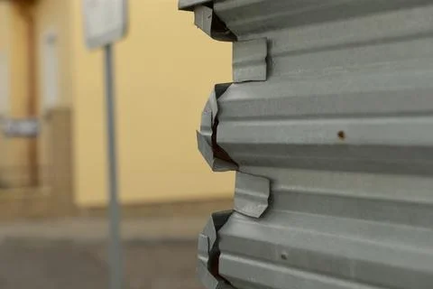 Close-up of dented corrugated metal shutter with urban background Stock Photos