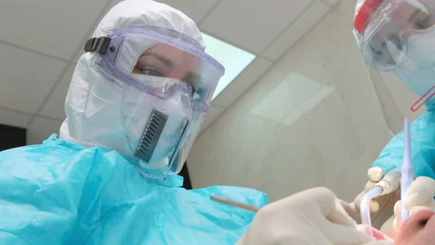 Close-up of dentist in a protective blue suit and assistant works with a patient Stock Footage 133563653