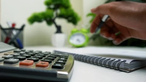 Close-up of a desk with a calculator, notebook, and a hand writing Stock Footage 316902087