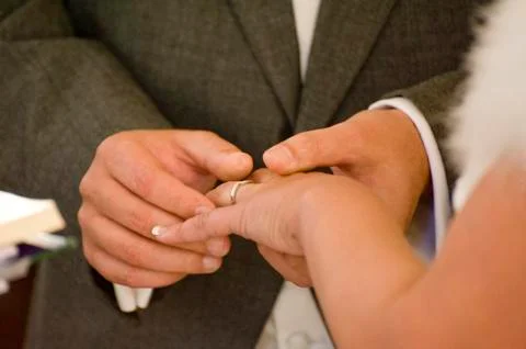 Close up detail of groom putting wedding ring on bride's finger during real c Stock Photos