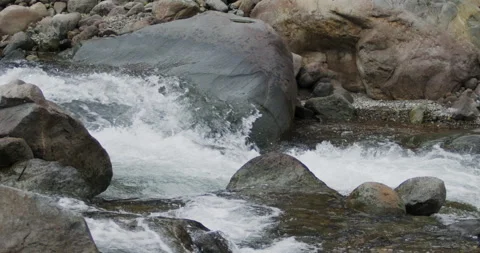 Close up detail of river water current flowing through river rocks in slow Video stock 240952409